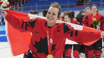 Marie-Philip Poulin élance le drapeau canadien dans les airs derrière elle, tandis qu'elle porte sa médaille d'or au cou gagnée lors de la finale contre les États-Unis à Beijing 2022