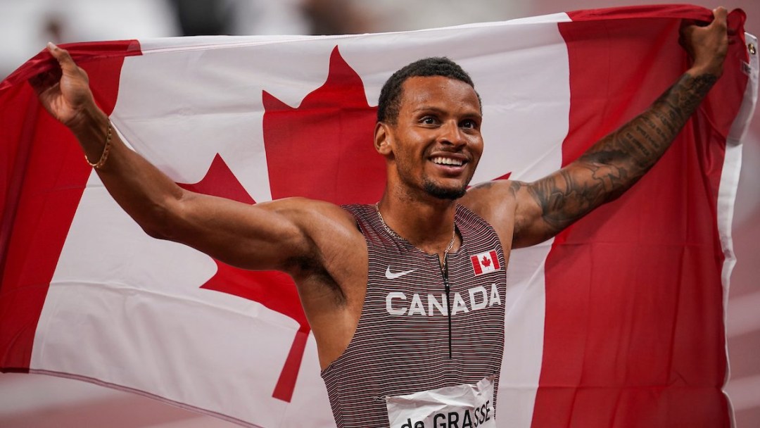 Andre De Grasse tient le drapeau canadien derrière lui.