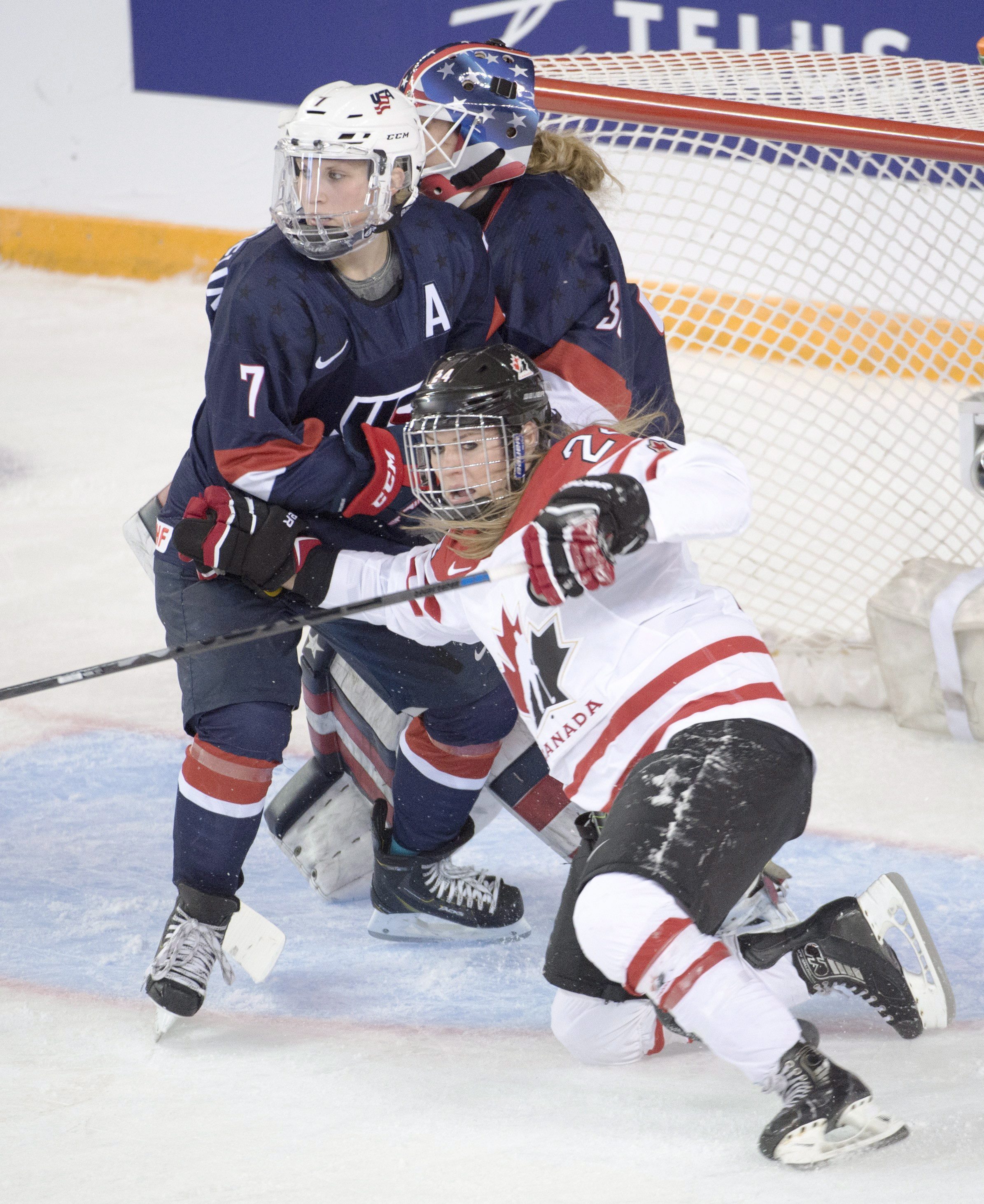 Natalie Spooner (24) est forcée au sol par Monique Lamoureux (7) des États-Unis devant la gardienne américaine Alex Rigsby en première période, le 28 mars 2016, à Kamloops (C.-B.). THE CANADIAN PRESS/Ryan Remiorz