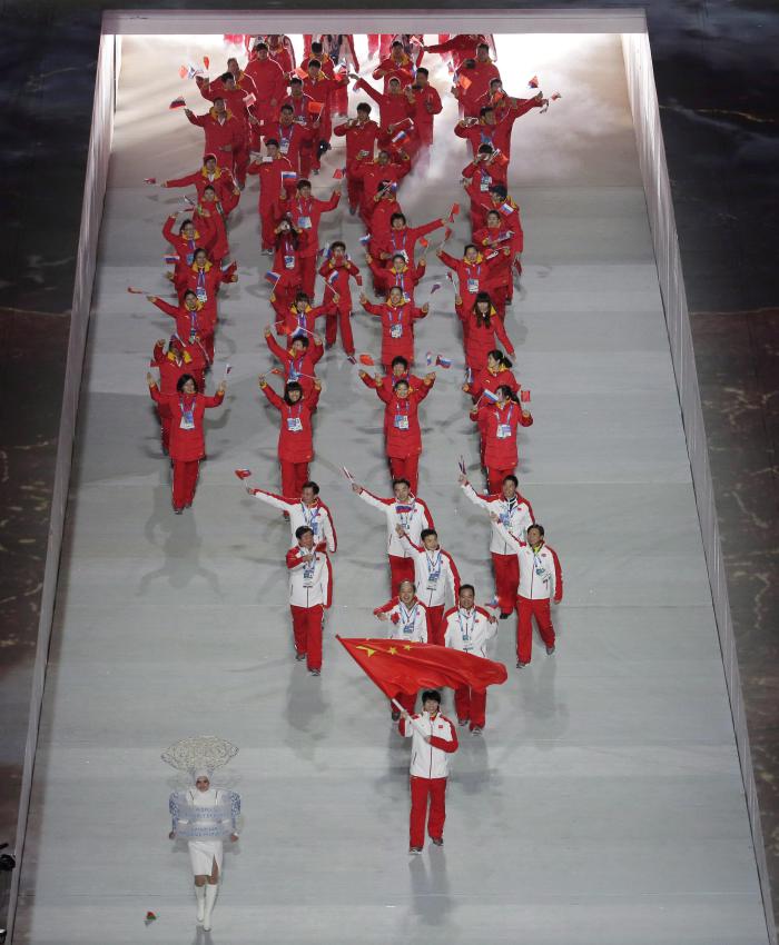 Tong Jian de Chine brandit son drapeau national et entre dans le stade avec ses coéquipiers lors de la cérémonie d'ouverture des Jeux olympiques d'hiver de 2014 à Sotchi, en Russie, le vendredi 7 février 2014. (AP Photo / Charlie Riedel)