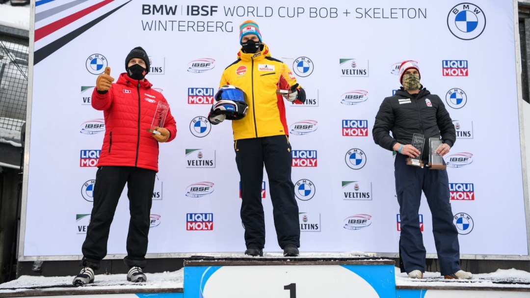 Justin Kripps sur la deuxième marche du podium aux côtés de Francesco Friedrich et de Benjamin Maier