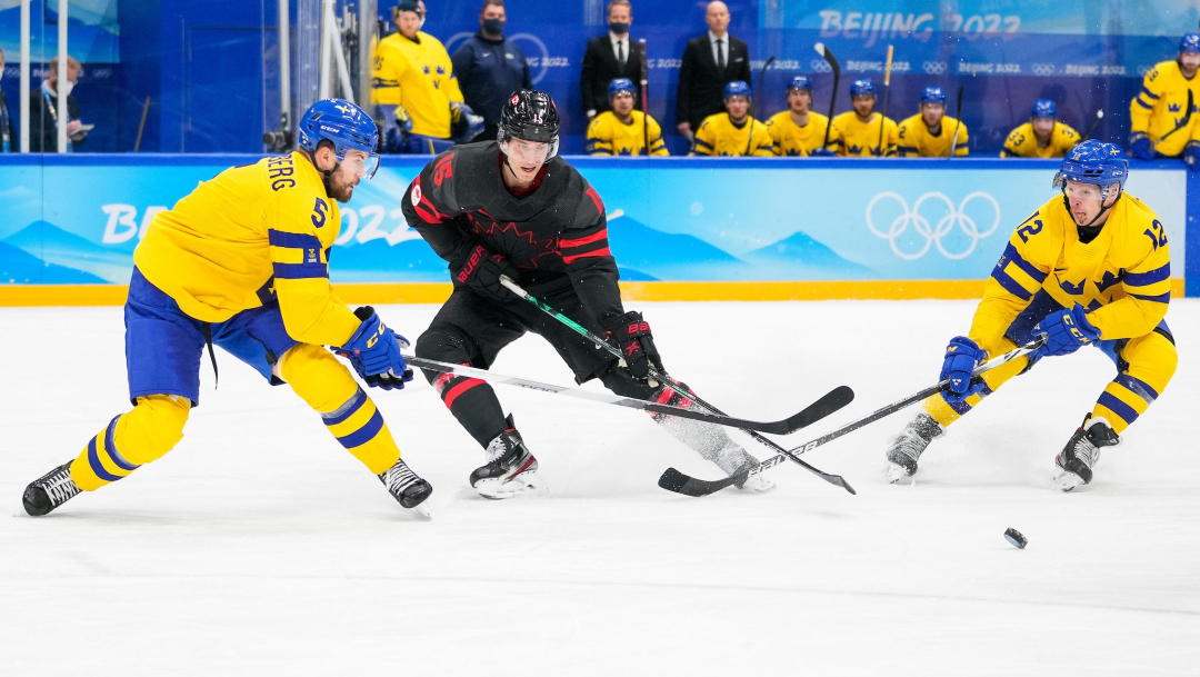 Un joueur de hockey fait une passe entre deux opposants sur la glace