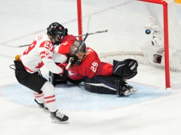 Seule devant le filet, l'attaquante du Canada Marie-Philip Poulin soulève la rondelle dans le haut du filet pendant que la gardienne suisse étend sa jambière et sa mitaine à Beijing 2022.