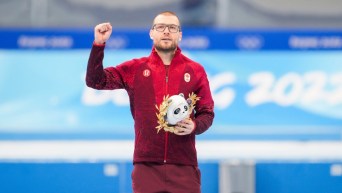 Laurent Dubreuil lève le point en l'air et tient la mascotte de Beijing 2022 dans l'autre main sur le podium, pour célébrer sa médaille d'argent en patinage de vitesse sur longue piste à l'épreuve du 1000 mètres masculin.