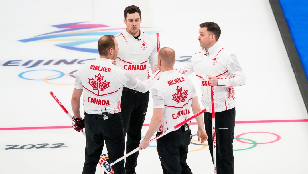 Brad Gushue donne la main haute à ses coéquipiers Brett Gallant, Geoff Walker et Mark Nichols après avoir battu l'équipe de la Norvège lors du tournoi à la ronde aux Jeux olympiques d'hiver de Beijing 2022. Ils sont en rond et tiennent d'une main leurs balais. Deux joueurs sont de dos alors que deux autres de face. Ils sont sur la glace et on voit le logo de Beijing 2022 sur la glace.