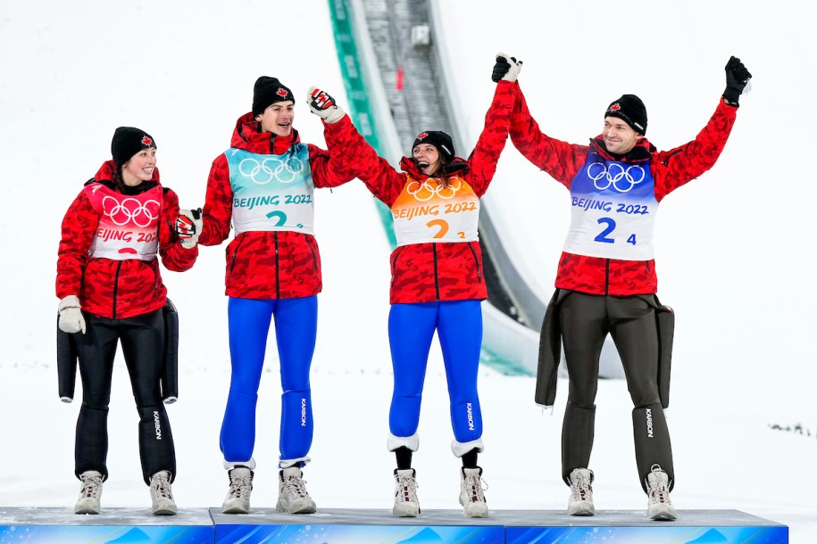 Les quatre canadiens médaillés de bronze en saut à ski à l'épreuve mixte par équipes sautent ensemble sur le podium