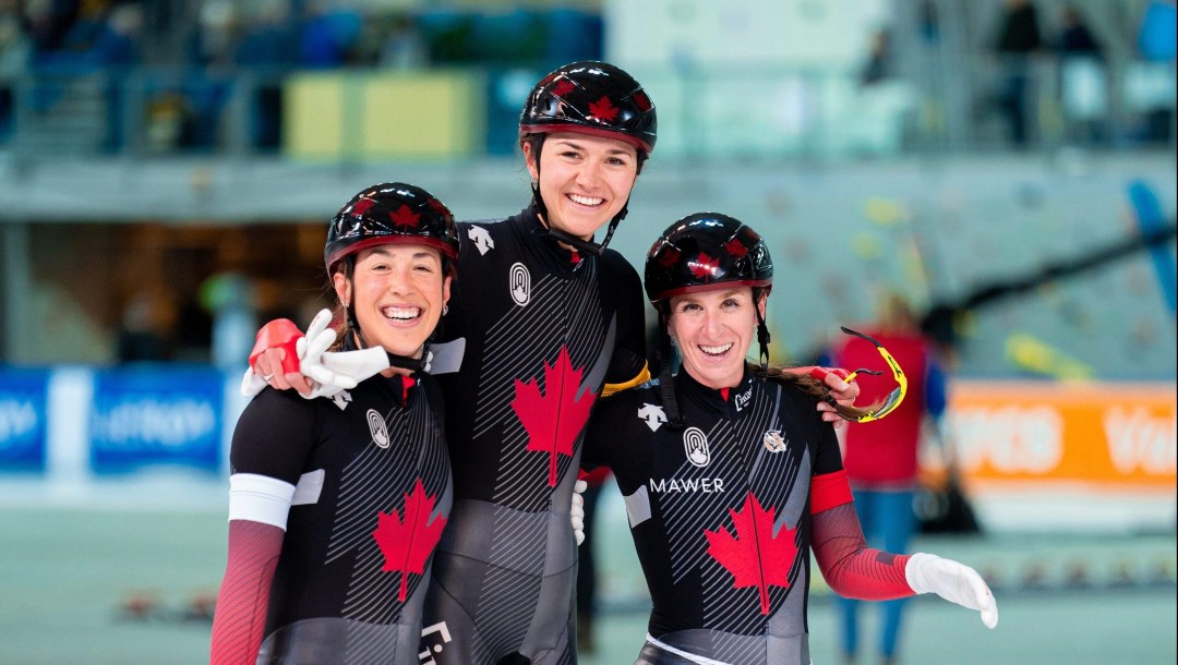 Trois patineuses canadiennes se tiennent par les épaules.