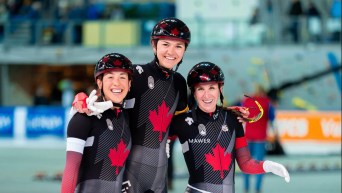 Trois patineuses canadiennes se tiennent par les épaules.