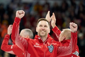 Brad Gushue sourit et lève les bras dans les airs.