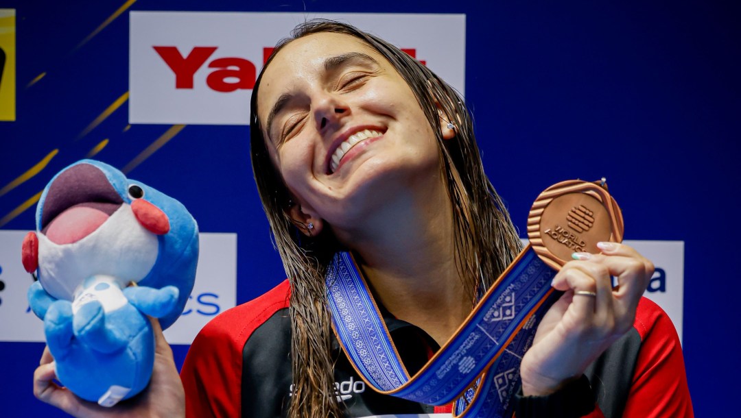 Pamela Ware sourit en tenant sa médaille et sa mascotte en peluche