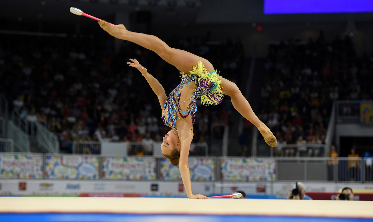 A rhythmic gymnast stands on one hand with her legs in a split holding a club
