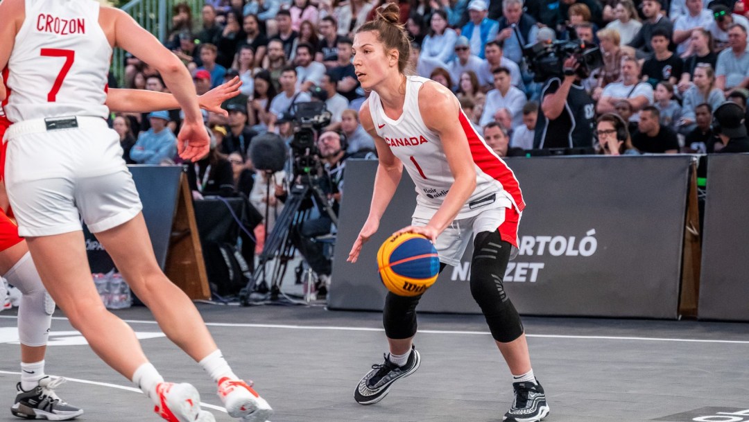 Michelle Plouffe in a white jersey and shorts dribbles a basketball