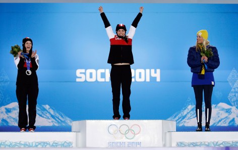 Marielle Thompson stands on the podium with both arms up, celebrating her gold medal victory at Sochi 2014