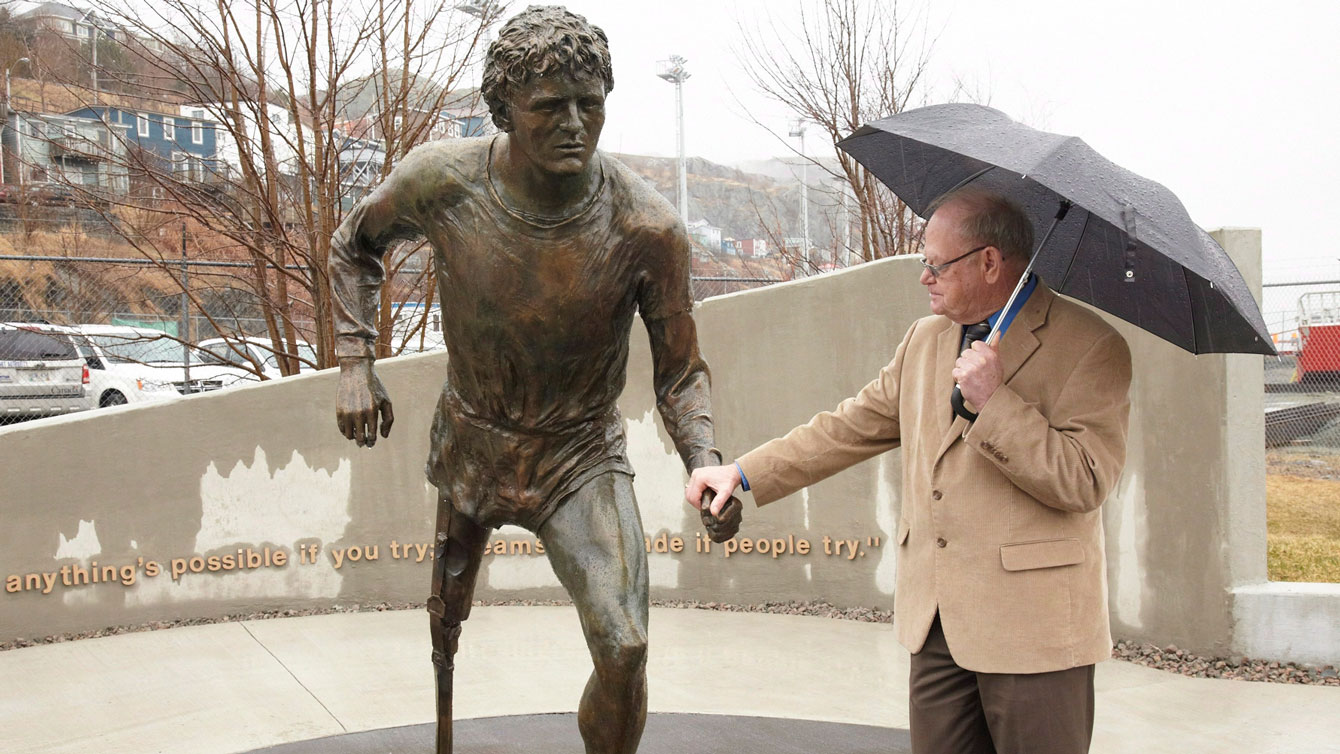 Rolland Fox with the statue of his son Terry at Mile 0 in St. John's, Newfoundland in 2012. One of Terry Fox's famous quotes, "I just wish people would realize that anything’s possible if you try; dreams are made possible if you try" is etched near the statue. 