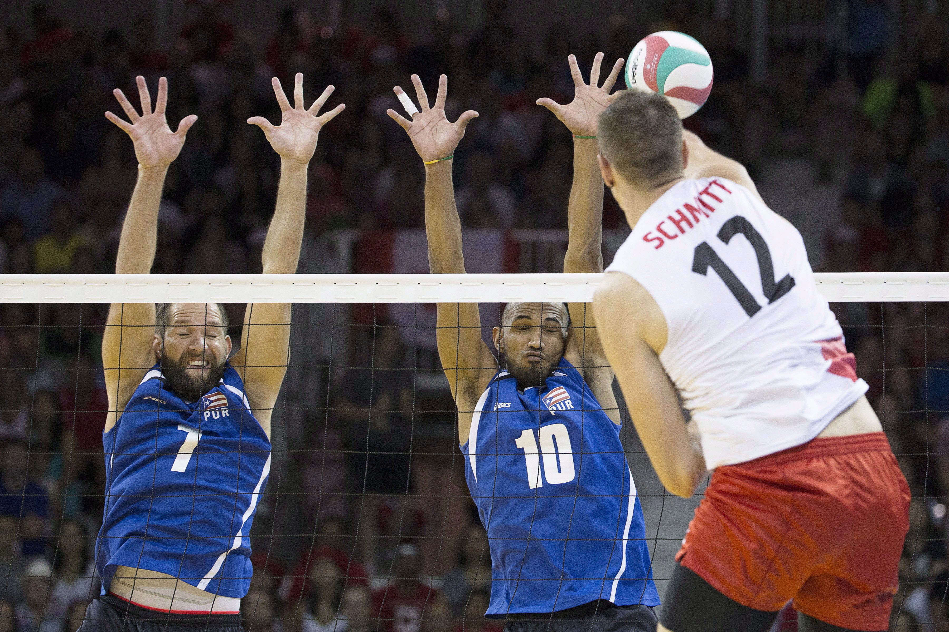 Puerto Rico's Enrique Escalante (left) and Ezequiel Cruz (centre) jump totry and block a spike from Canada's Gavin Schmitt