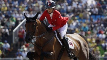 A female equestrian in a red jacket rides a brown horse