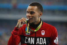 Andre De Grase bites his silver medal on the podium