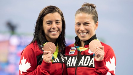 Pair smiling with Olympic bronze medals in hand looking at camera