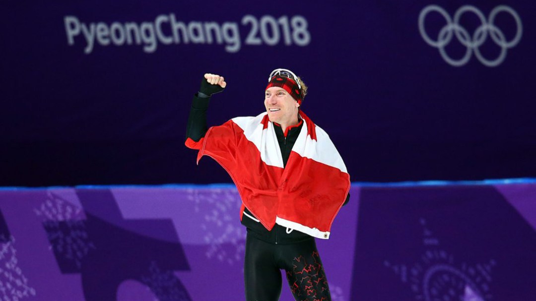 Ted-Jan Bloeman waves to the crowd with a Canadian flag wrapped around him after winning gold in the men's 10000m final at the 2018 winter Olympics.