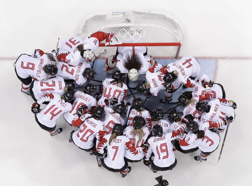 Overhead shot of Team Canada women's hockey players around the net
