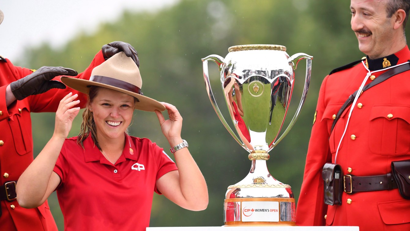 Brooke Henderson puts on a Mountie hat while standing next to a trophy
