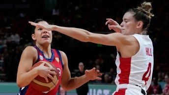 Sami Hill in a white basketball uniform puts her arm out to block an opponent with the ball