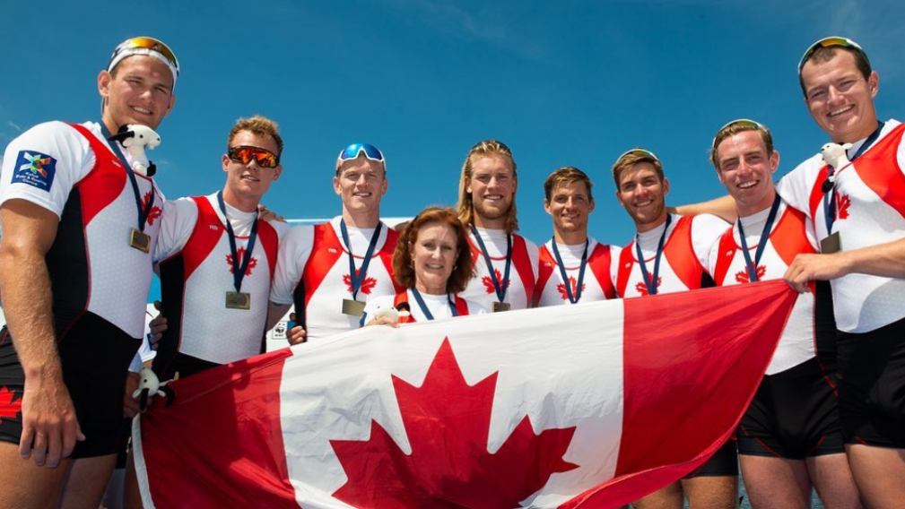 Team Canada standing in front of flag with bronze medals.