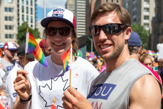 Anastasia Bucsis and Dylan Moscovitch wave small Pride flags at the 2017 Toronto Pride parade.