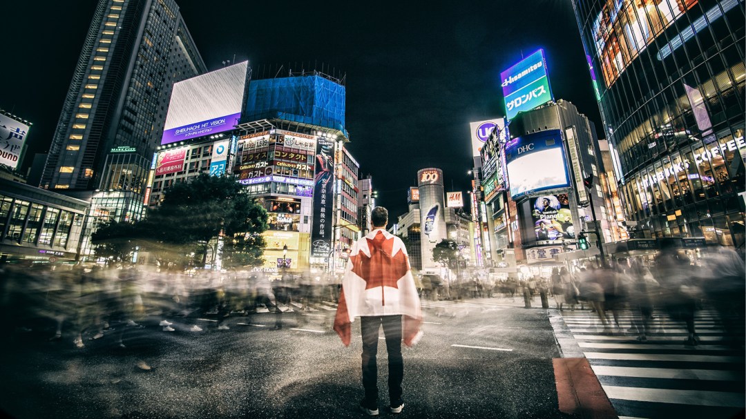 Person draped in Canadian flag stands in Tokyo