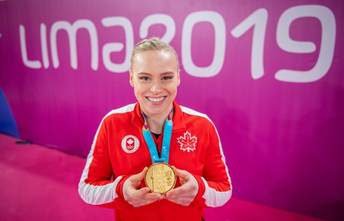 Athlete poses with her gold medal in front of Lima 2019 sign