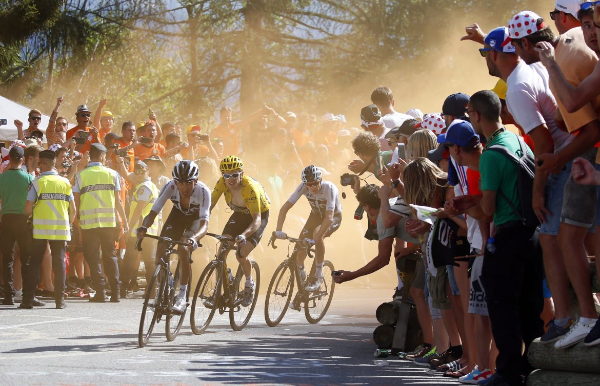 Three cyclists riding around corner with large crowds on both sides