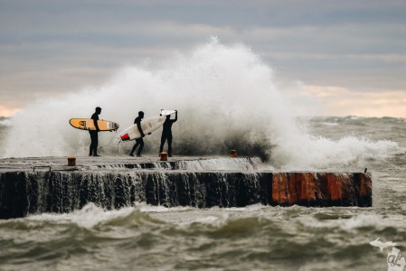 Three surfers in thick wetsuits bracing for a wave