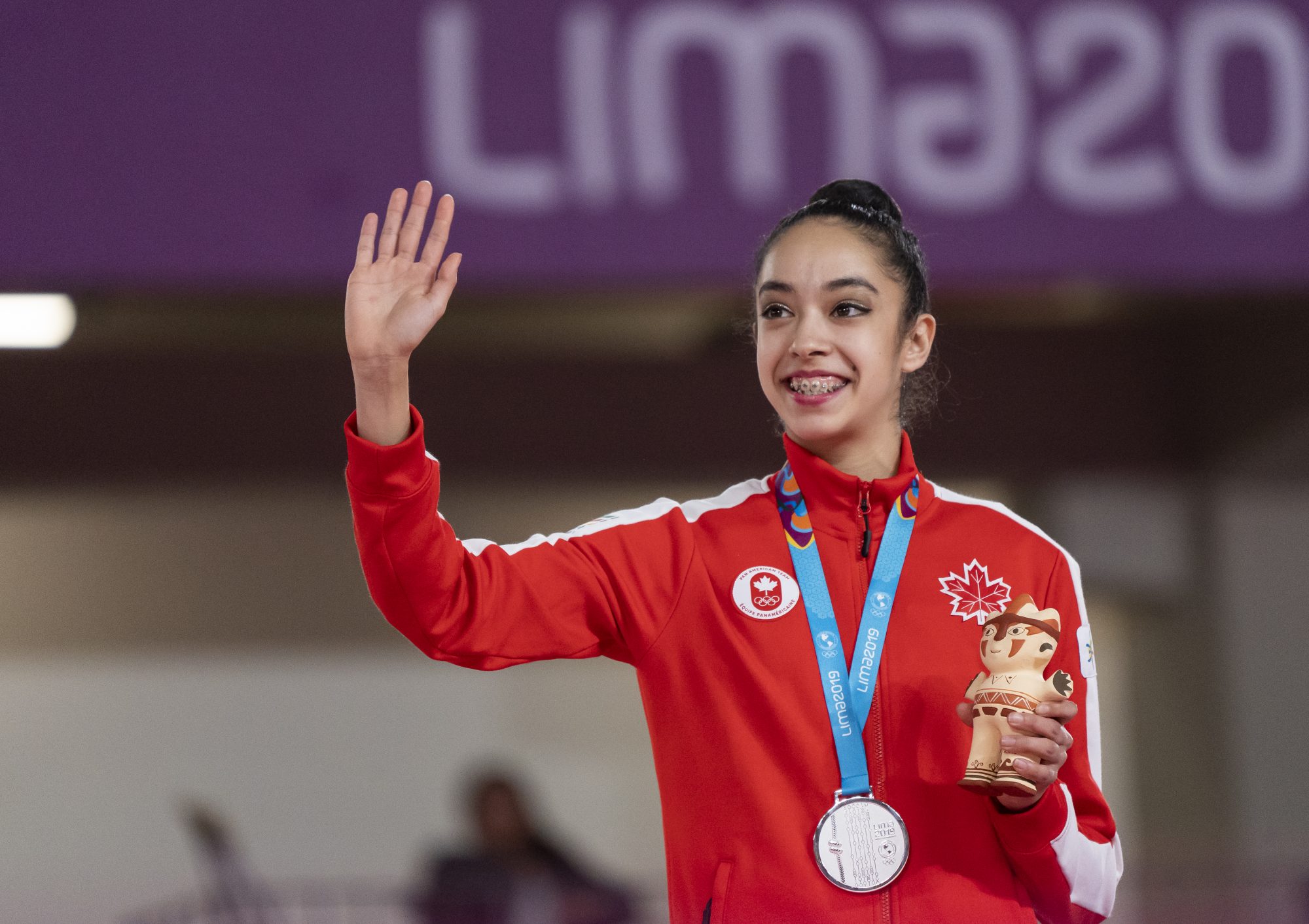 athlete waves while wearing her medal