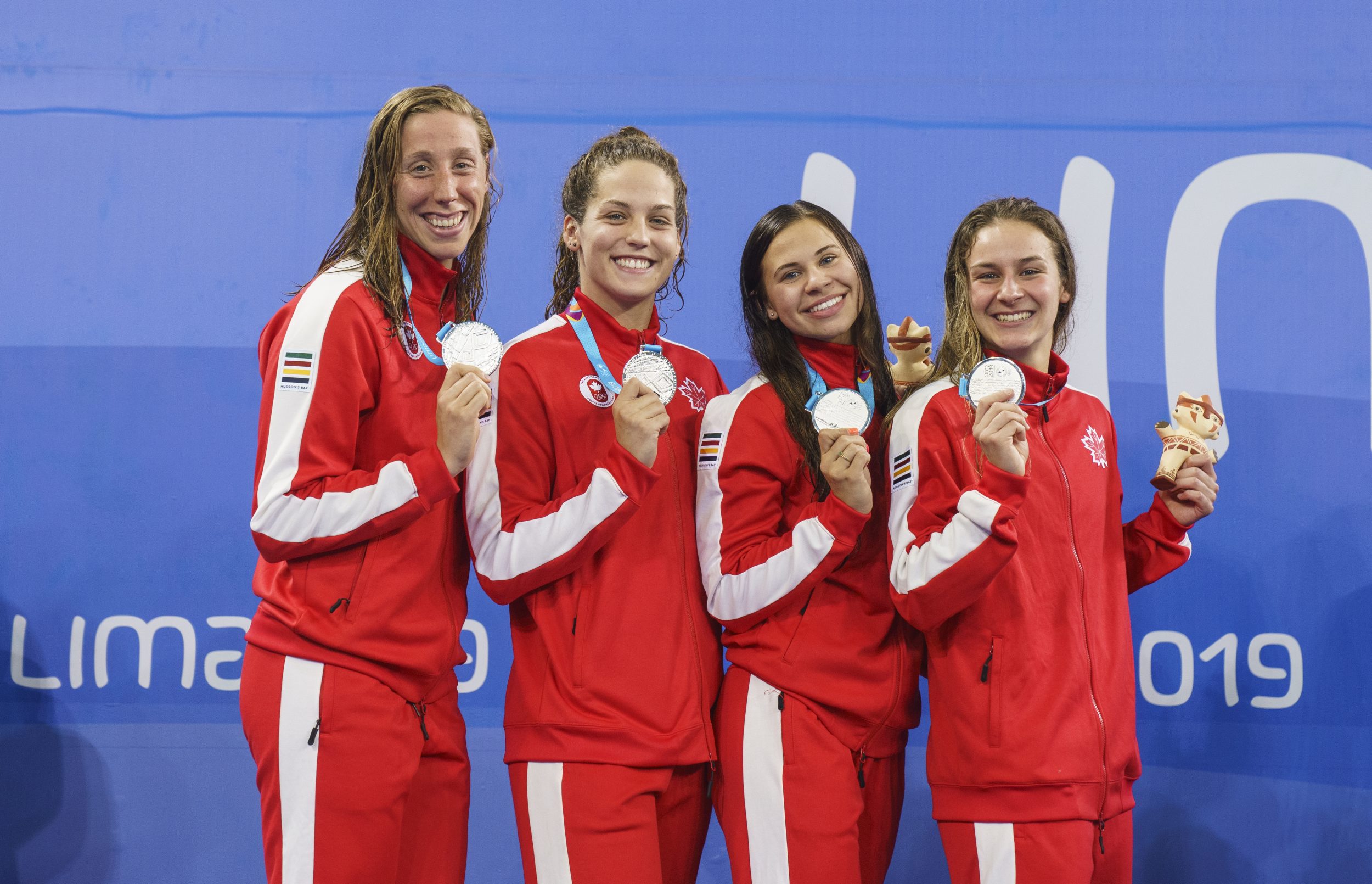 four swimmers stand on the podium holding silver medals