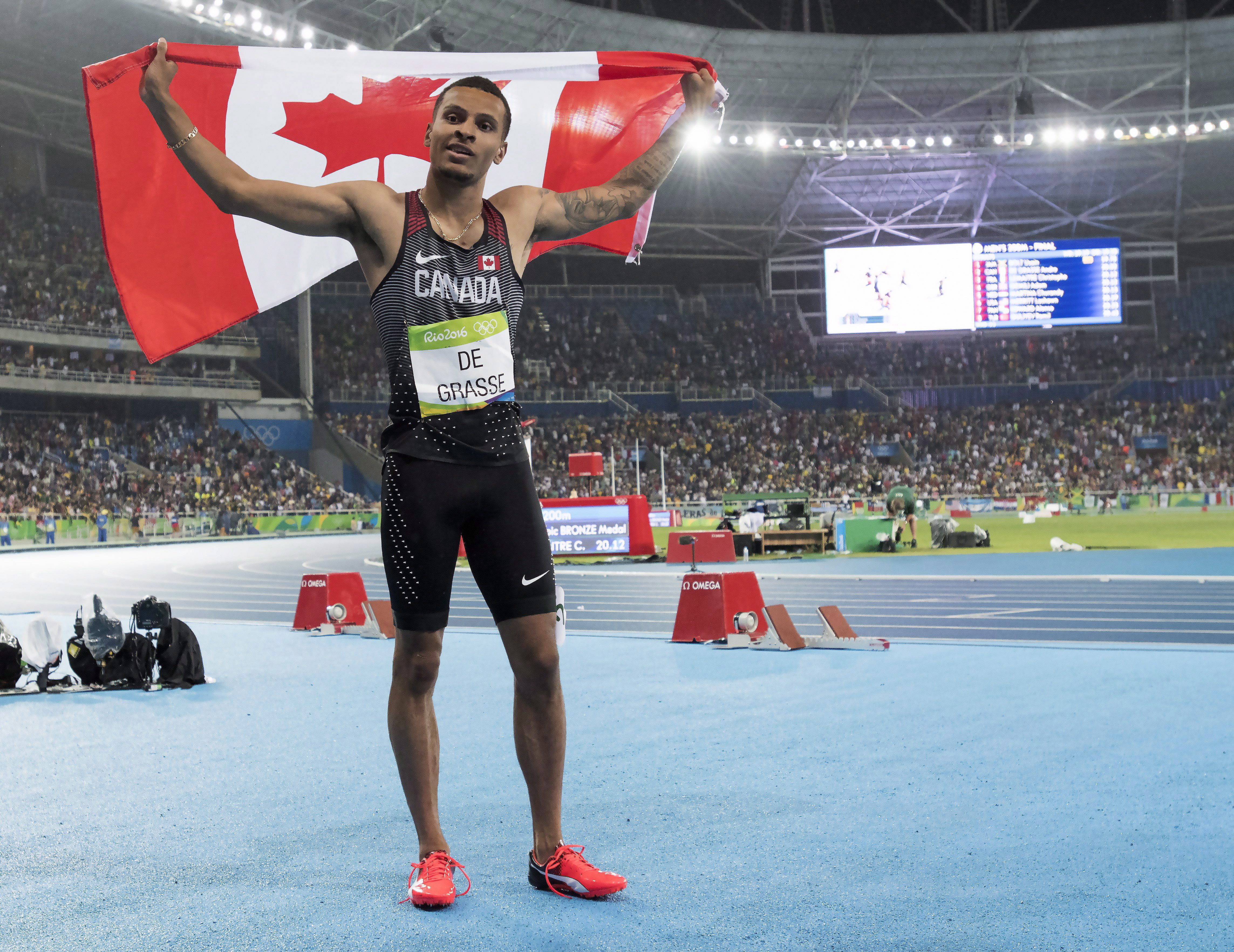Andre De Grasse holds the Canadian flag over his head celebrating his Silver medal win.