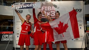 Canada's 3x3 team celebrates their victory with Paige (far left) and Michelle holding a '3x3 Edmonton 2019 Winner' sign, and Catherine and Katherine (far right) holding the Canadian flag.