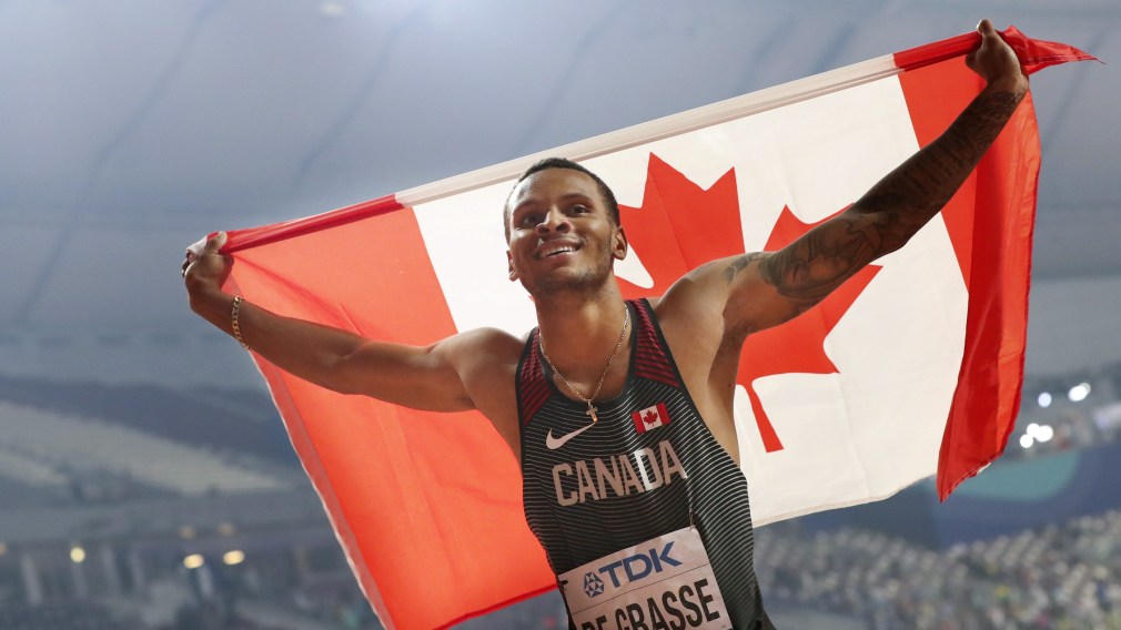 Andre De Grasse holds the Canadian flag up behind him.