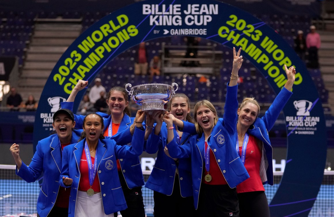 Canada's tennis team hold up the Billie Jean King Cup trophy while  wearing blue blazers