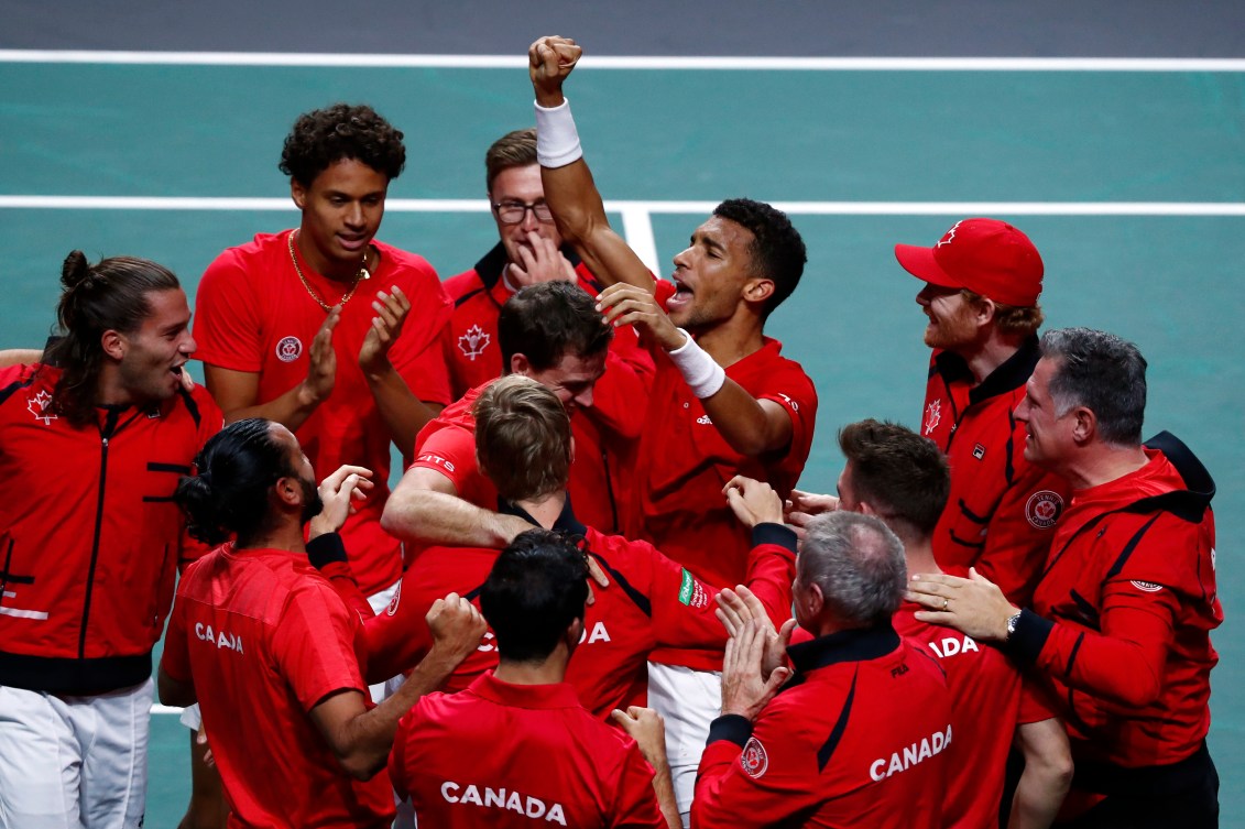 Felix Auger-Aliassime raises his arms in celebration while being mobbed by teammates 