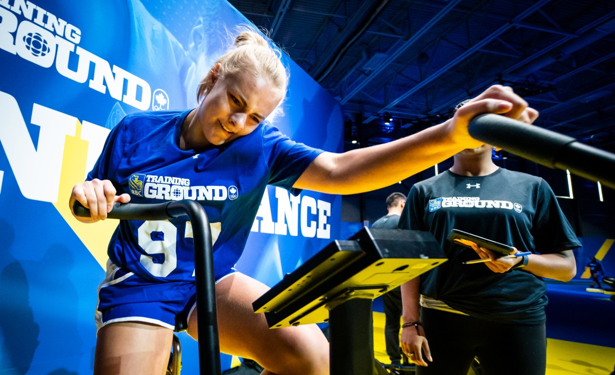 A female athlete rides the bike at the endurance station.