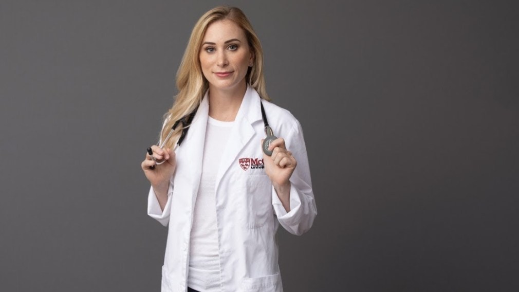 Joannie Rochette holds a stethoscope over her shoulders, posing for a photo in her white doctor's coat.
