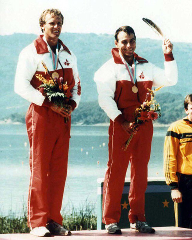 Alwyn Morris holds an eagle feather on the Olympic podium alongside Hugh Fisher