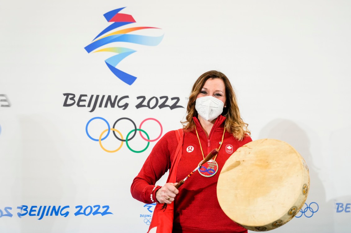 Catriona Le May Doan poses with an Indigenous drum in front of the Beijing 2022 emblem