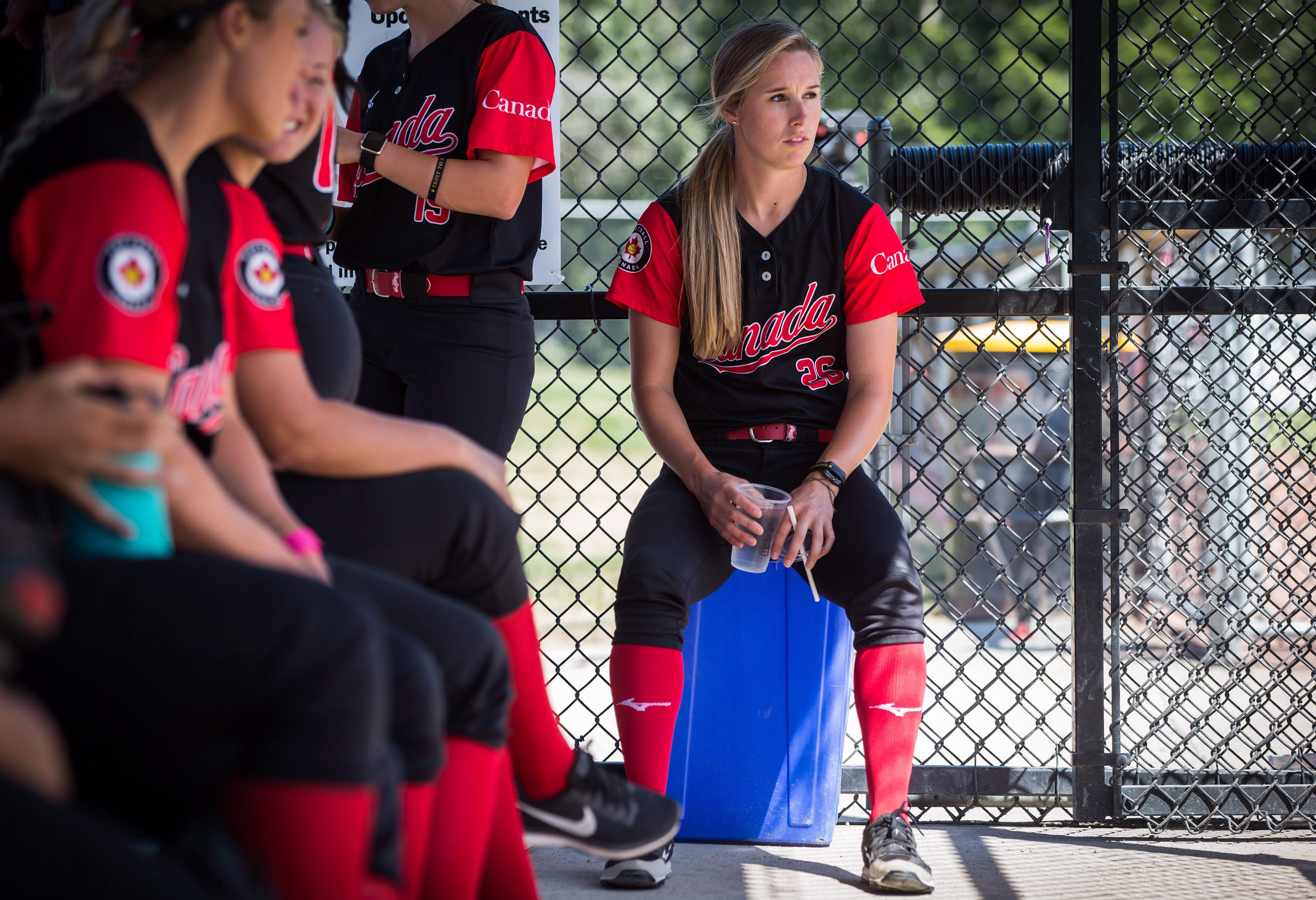 Softball player sits in dugout with teammates