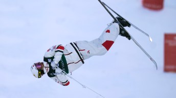 Kingsbury mid-turn in the air, hugs his arms close to his chest while his skis are in the air.