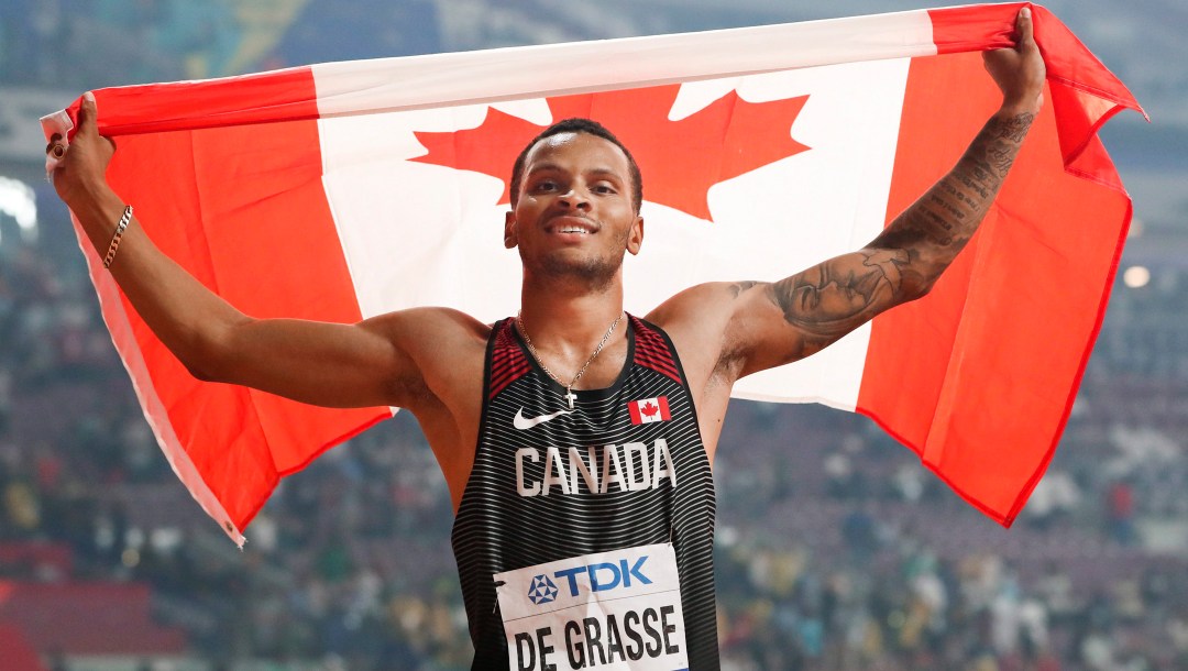 Andre De Grasse holds up the Canadian flag behind his head.