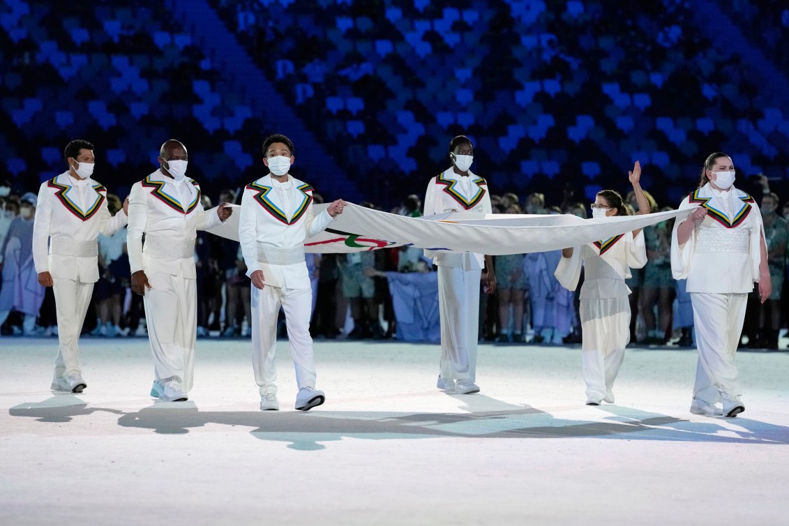 Six athletes carrying Olympic flag.