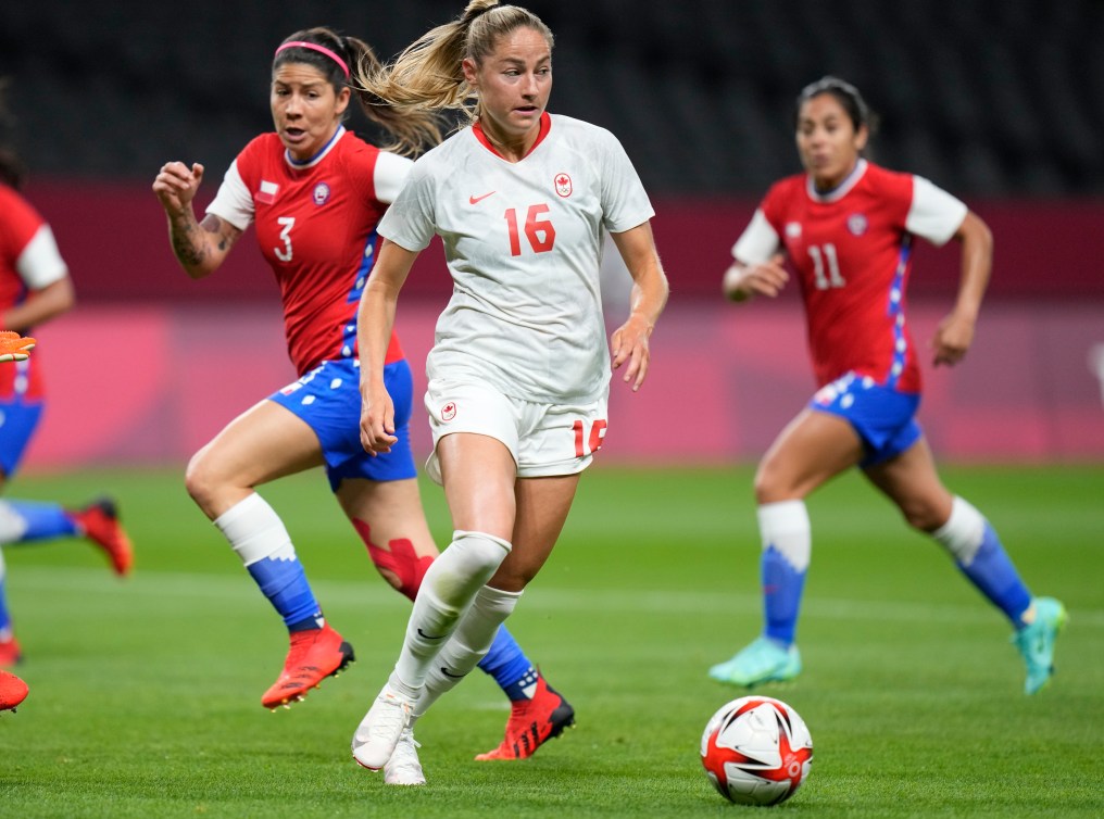 Canadian player Janine Beckie controls the ball at her feet, with two Chilean players in the background.