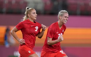 Soccer player Adriana Leon, alongside teammate Sophie Schmidt, holds up the Canada crest on her jersey.