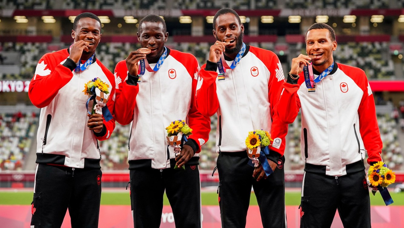 Men's 4x100m relay team bite their medals on the podium